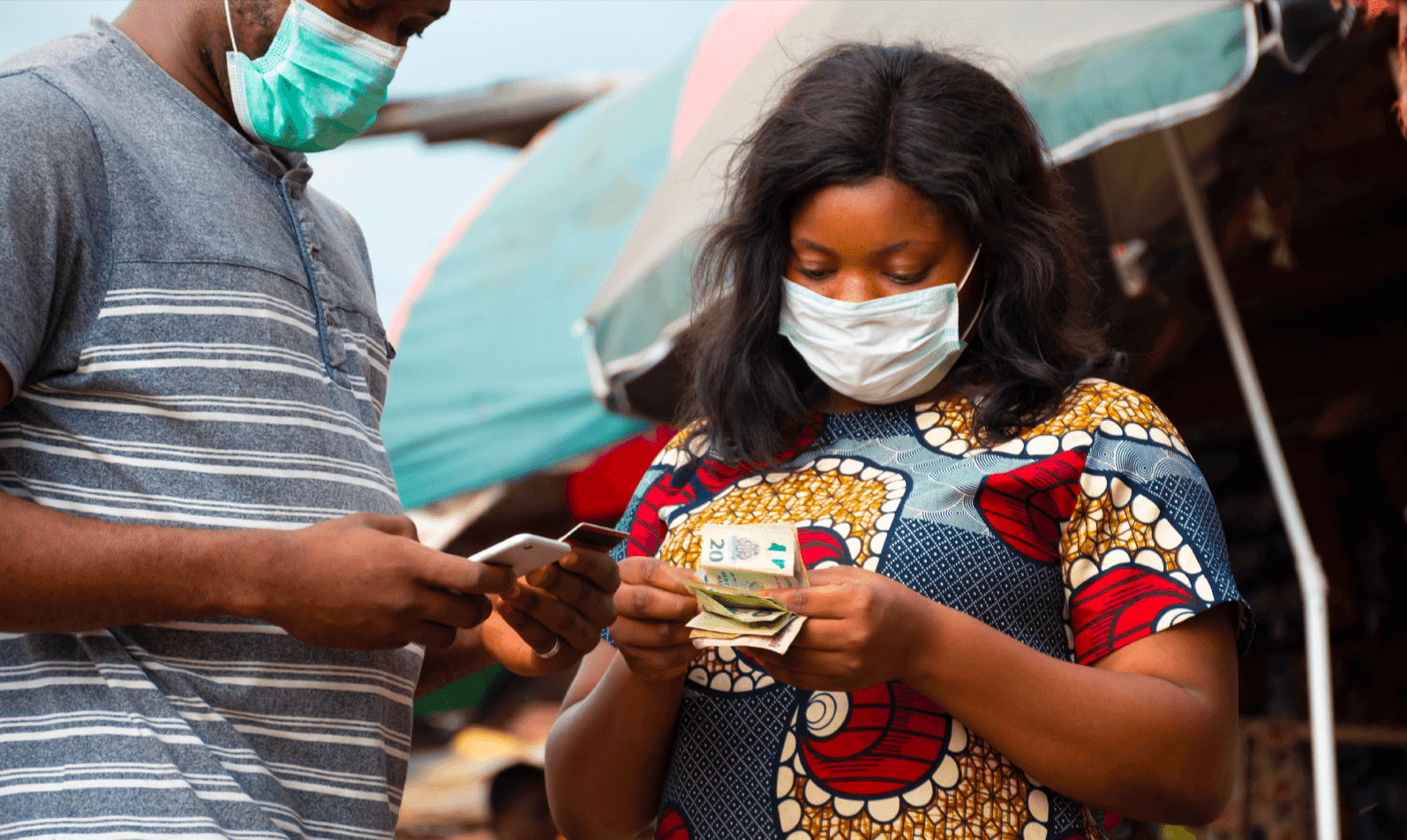 People with masks on, one holds a phone while the other holds money